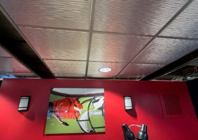 Framed Photo on a Red Wall Between Two Wall Sconces with Ceiling Panels Above and Two Black Lamps in the Foreground