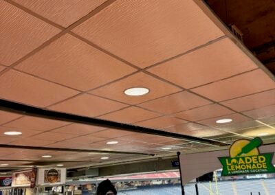 Concession Area in a Stadium Concourse with White Counters Coolers and a Bright Loaded Lemonade Sign Empty Seats Visible Beyond