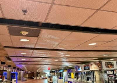 Long Indoor Hallway with Beige Tiled Ceiling Recessed Lights and Snack Shops Along the Right Side