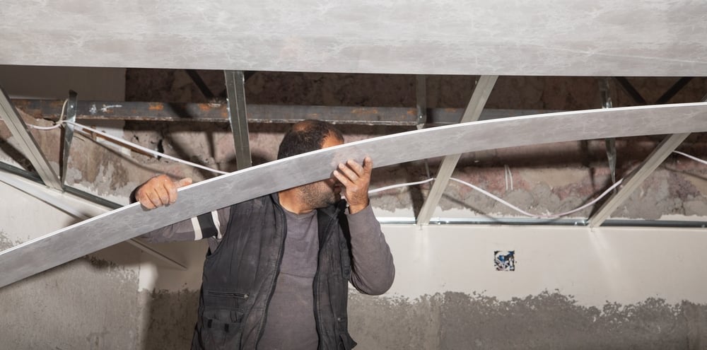 Construction workers installing a suspended ceiling grid system in a commercial building interior.