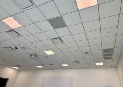 Ceiling View of a White Tiled Room with Recessed Lights and Vents a Whiteboard Mounted on the Far Wall