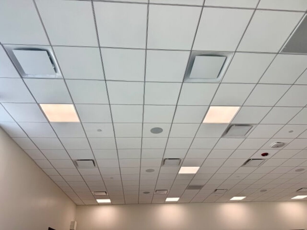 Drop Ceiling with White Square Tiles Recessed Lights Vents and Diffusers in a Large Empty Room from a Low Angle