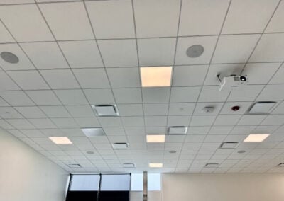 Ceiling Grid with Square Tiles Recessed Lights Vents and a Ceiling mounted Projector Windows Along the Far Wall Reveal Natural Light