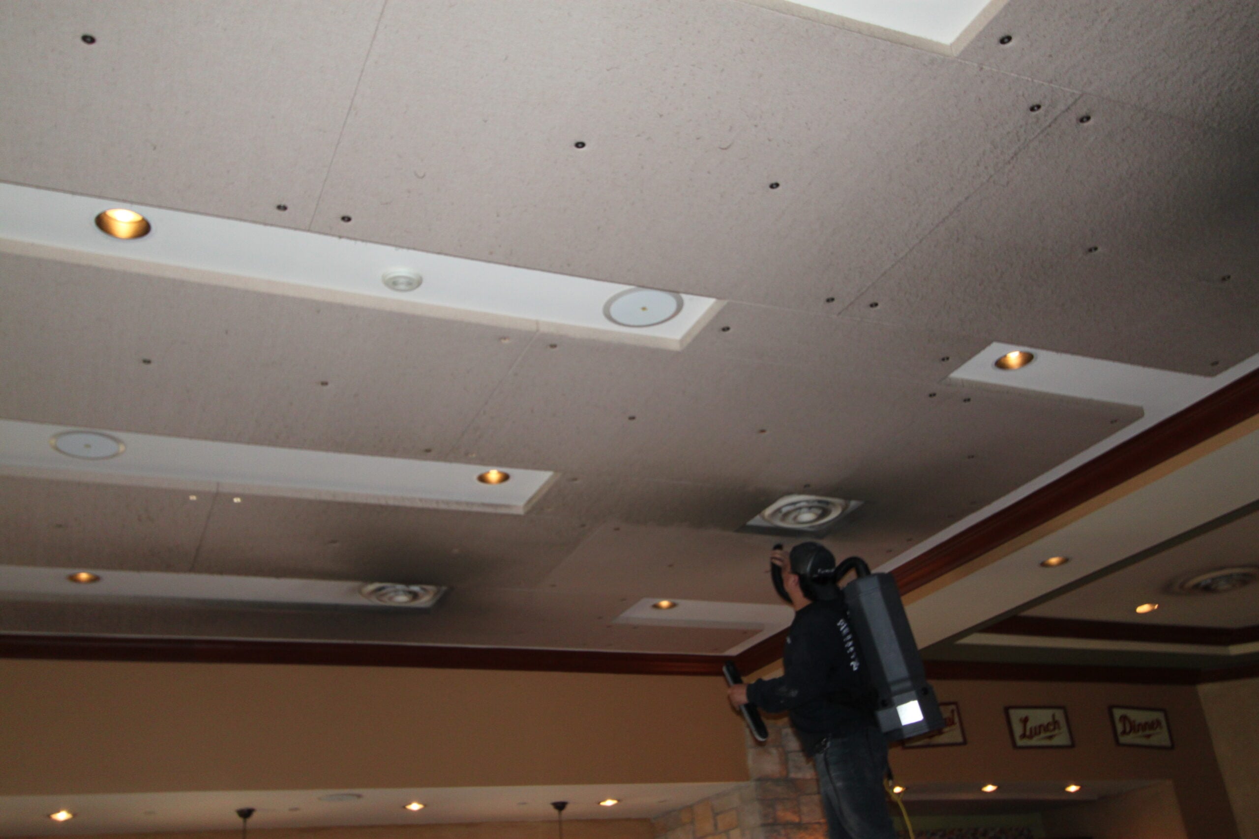 IMG_2354 Professional technician inspecting and cleaning dirty commercial ceiling tiles using specialized equipment to improve indoor air quality and maintain a clean business environment.